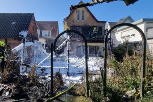 Löscharbeiten der Feuerwehr an einem brennenden Wohnhaus mit starkem Rauch und sichtbaren Schäden.