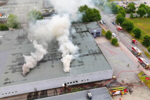 Brand in Lagerhalle, starke Rauchentwicklung, Feuerwehr im Einsatz, Drohneneinheit unterstützt Brandbekämpfung.