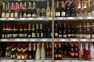 Sektflasche im Vordergrund, Finanzthemen im Hintergrund, alkoholsteuerliche Anhebung wird angezeigt.