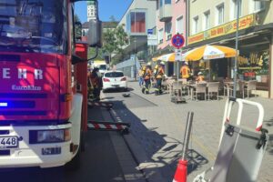 Feuerwehr löscht Küchenbrand in Restaurant, Einsatzfahrzeuge sichtbar, Rauch und Schläuche im Hintergrund.