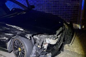 Ein beschädigter Mercedes-Benz, Unfallstelle mit Polizei und Pfefferspray-Angriff im Hintergrund.