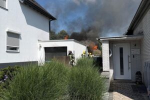 Feuerwehrleute im Einsatz bei Garagenbrand in Witten-Heven, Riegelstellung gegen Brandausbreitung.