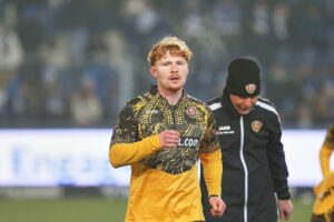 Robert Wagner in Dynamo Dresden-Trikot, feierlich, mit Fußball im Hintergrund.