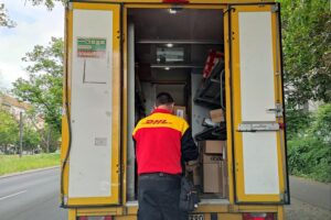 Ein Paketfahrer mit schweren Paketen vor einer Zustellstelle, symbolisch für Arbeitsschutz und Gesundheit.