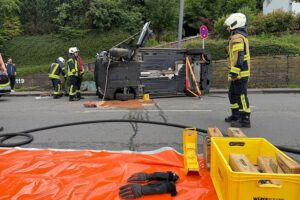 Unfallfahrzeug auf der Seite liegend, Feuerwehrleute befreien den eingeklemmten Fahrer.
