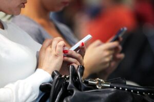 Zwei Frauen nutzen Smartphones, symbolisieren digitale Medienerziehung und elterliche Verantwortung in der Gesellschaft.