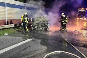 Feuerwehr löscht brennendes Fahrzeug nach schwerem Autobahnunfall, Verletzte werden versorgt.