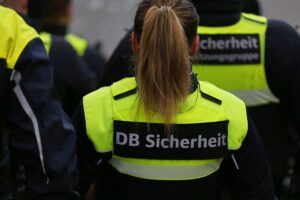 Zugbegleiter kontrolliert Fahrscheine; aggressive Reaktion eines Passagiers im Fokus der Szene.
