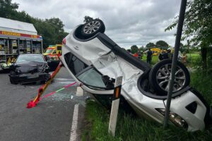 Zwei beschädigte Fahrzeuge an einer Kreuzung, Feuerwehr und Rettungsdienste vor Ort.