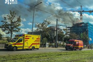 Dachstuhlbrand in Dresden: Feuerwehr und Einsatzwagen vor brennendem Gebäude, Rauchentwicklung, Dachhaut wird geöffnet.