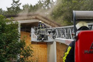 Feuerwehrleute löschen Brand in ehemaligem Schulgebäude, Rauch dringt aus dem Fenster.
