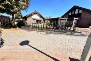 Feuerwehr löscht Heckenbrand, schützt Garage, Einsatzkräfte arbeiten unter Atemschutz, verletzte Person versorgt.