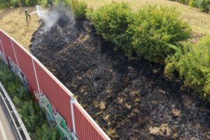 Feuerwehr löscht Böschungsbrand an der A40, Einsatzkräfte mit Ausrüstung, Rauch und Flammen sichtbar.
