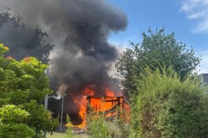 Ausgebrannte Gartenhütte in Bad Bederkesa, Feuerwehr im Einsatz, Flammen und Löscharbeiten am Hang.