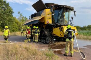 Feuerwehr löscht brennenden Mähdrescher bei Erntearbeiten, starke Rauchentwicklung am Schneidwerk (Archiv).