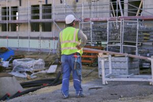 Bauarbeiter auf einer Baustelle im Hintergrund, Baustelle mit Baufahrzeugen und Wohngebäude im Entstehen.