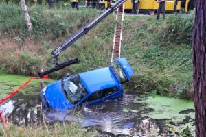 Ein Abschleppkran hebt einen im Oste-Hamme-Kanal abgestürzten VW Polo; Feuerwehr legt Ölsperre aus.