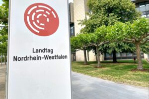 Sitzung im Landtag Nordrhein-Westfalen zur Hitzewelle und gesundheitlichen Rückwirkungen, symbolisiert durch Politiker.