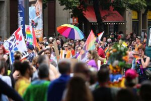 Ulf Kämpfer auf CSD, umgeben von bunten Fähnchen und fröhlichen Menschen, feiert Vielfalt.