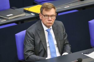 Johann Wadephul in Anzug, bei Pressegespräch, im Hintergrund NATO-Flaggen, symbolisiert internationale Sicherheit.