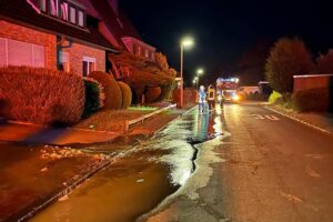 Wasserrohrbruch, Feuerwehr im Einsatz, abgesperrte Straße, Wasser auf Gehsteig, keine Verletzten.