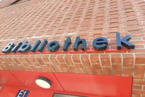 Bibliothek mit offenen Regalen, Besuchern, die Bücher durchsehen und eine einladende Atmosphäre genießen.
