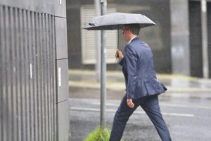 Mann mit Regenschirm vor wechselhaftem Wetter, symbolisiert Regen und windige Bedingungen in Niedersachsen.